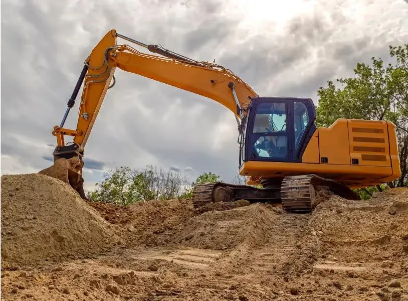 Orange excavator digging into a mound of dirt on a land clearing site