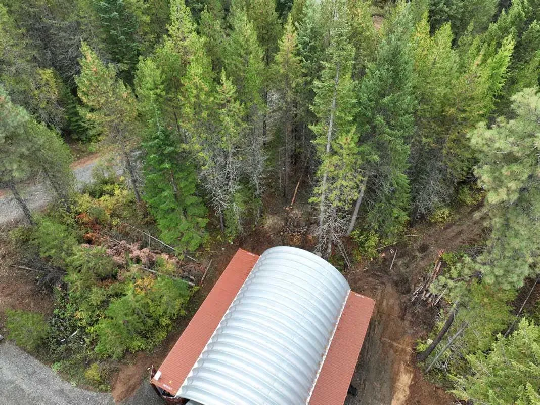 Aerial view of defensible space cleared around an arched metal building in the forest